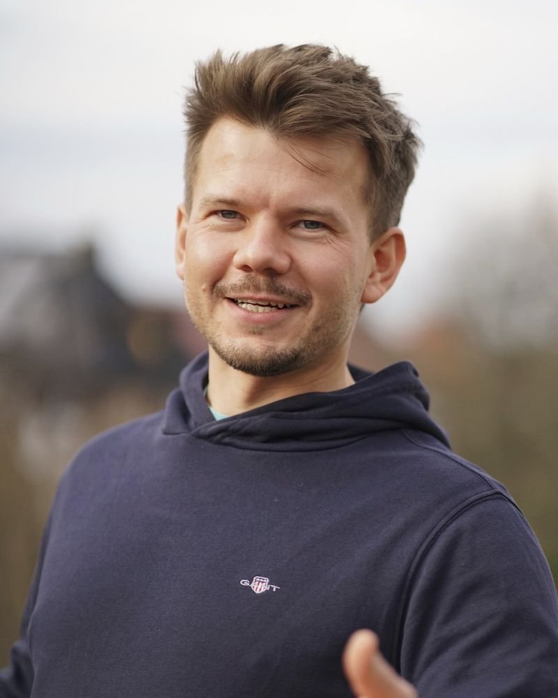 Ertmann Buchholz, Coach und Trainer aus Münster, lächelt und lädt mit offener Handgeste ins Gespräch ein